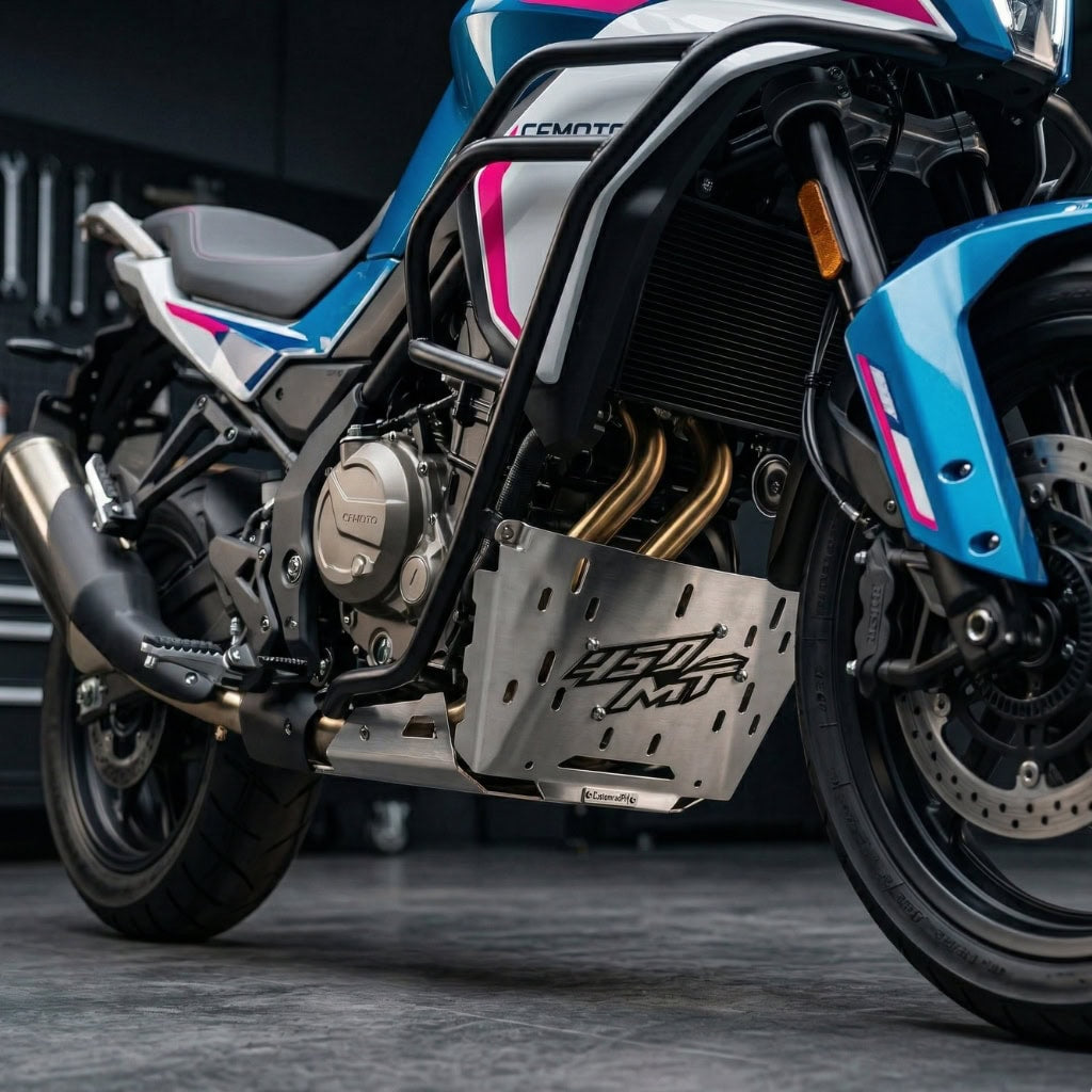 A detailed close-up photograph of the brushed silver CNC steel CustomradPH belly pan cover, featuring a distinctive raised "450 MT" logo, installed on the lower section of a CFMOTO 450MT motorcycle. The cover is mounted cleanly below the engine's exhaust headers and behind the front wheel, set against a blurred workshop background to highlight the product's precise fitment.